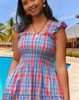 Woman wearing a plaid Angele H Paris tiered ruffle shoulder dress by a pool with a tropical background